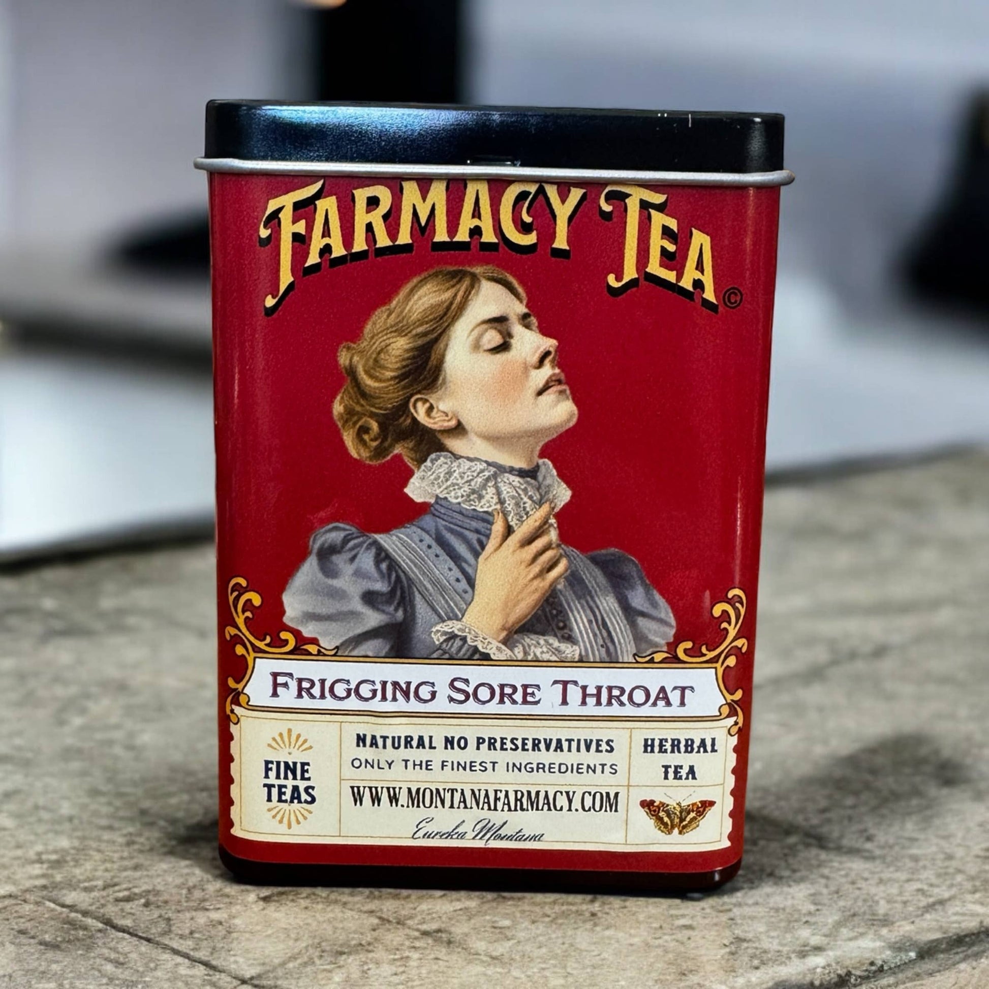 Red tin canister of Farmacy Tea with vintage-style label featuring a woman and text.