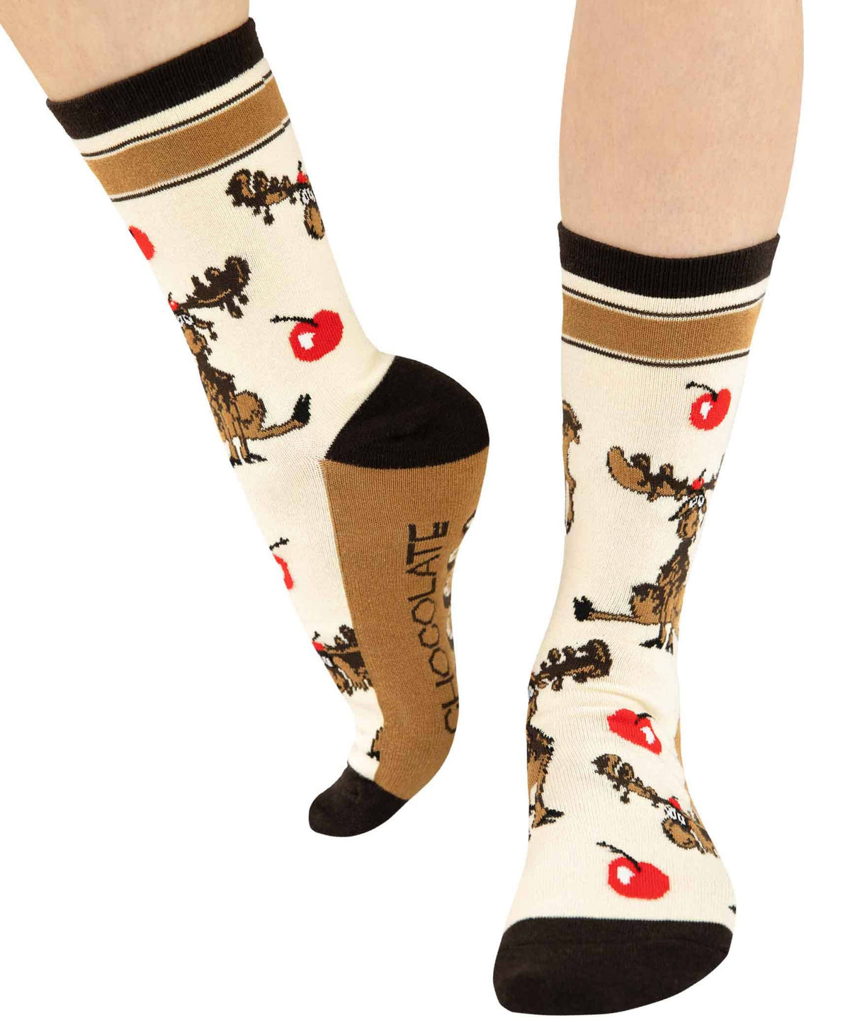 A pair of crew socks worn on a person's legs, featuring a cream background with brown moose prints, red cherries, and dark toe/heel/cuff details. The word 'CHOCOLATE' is printed vertically on the sole of one sock.