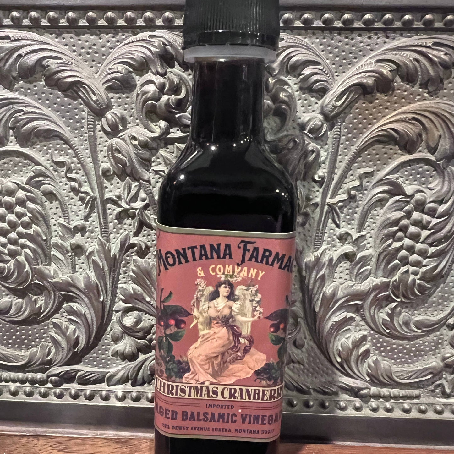 Bottle of Montana Farmacy & Company Christmas Cranberry Balsamic Vinegar on a decorative surface.