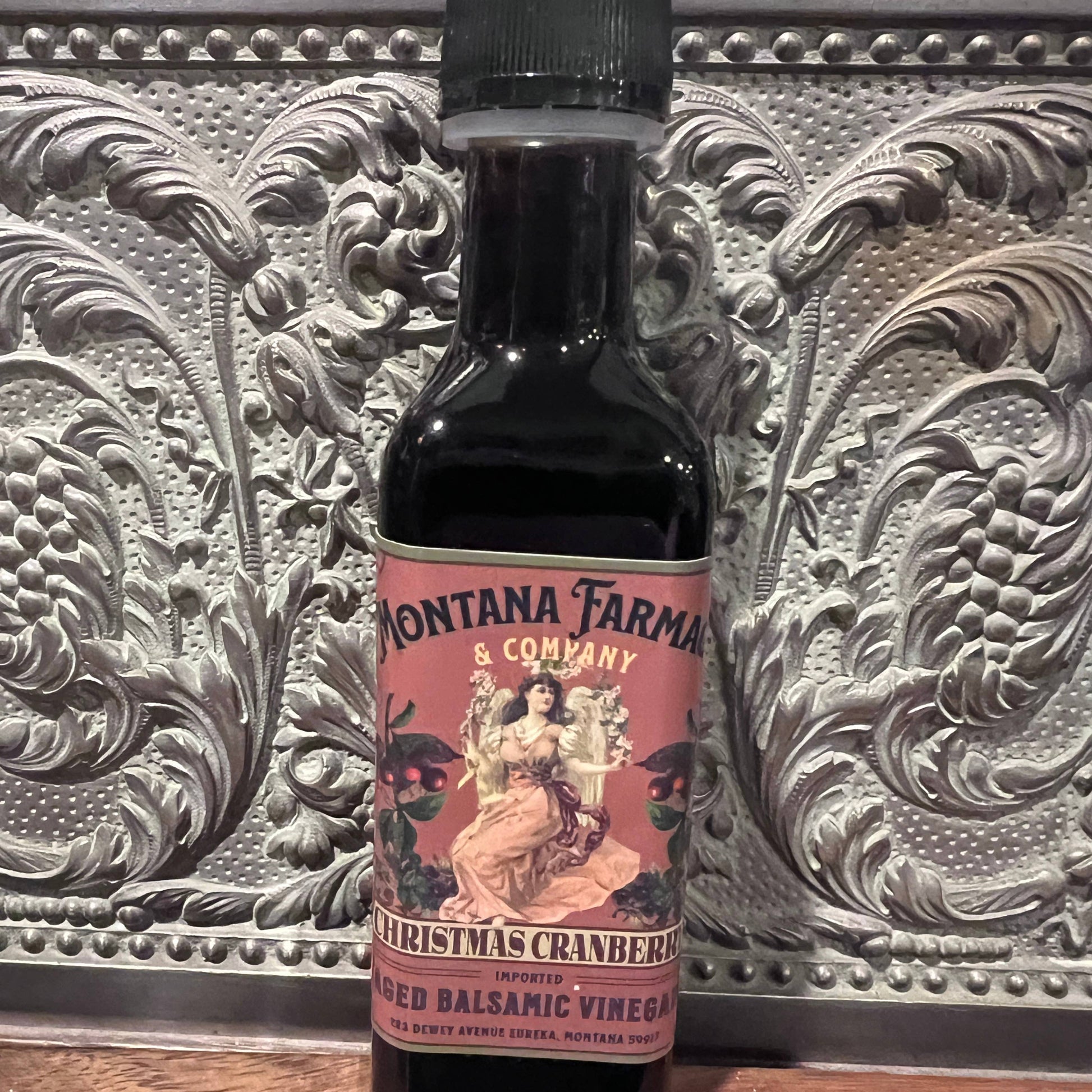 Bottle of Montana Farmacy & Company Christmas Cranberry Balsamic Vinegar on a decorative surface.