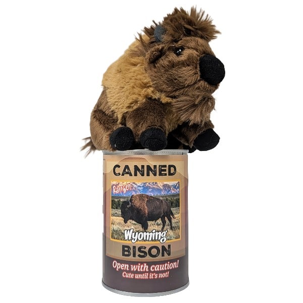 A plush toy bison stuffed animal with brown and tan fur, black hooves and snout, and small gray horns, sitting on a can labeled 'Canned Wyoming Bison' photographed on a plain white background.