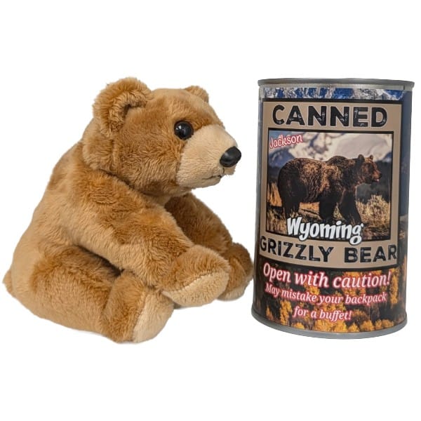 A plush brown grizzly bear toy sitting next to a cylindrical metal can labeled 'Canned Wyoming Grizzly Bear' on a plain white background.