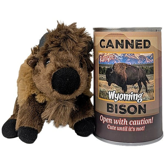 A plush toy bison stuffed animal with brown and tan fur, black hooves and snout, and small gray horns, sitting beside a can labeled 'Canned Wyoming Bison' photographed on a plain white background.